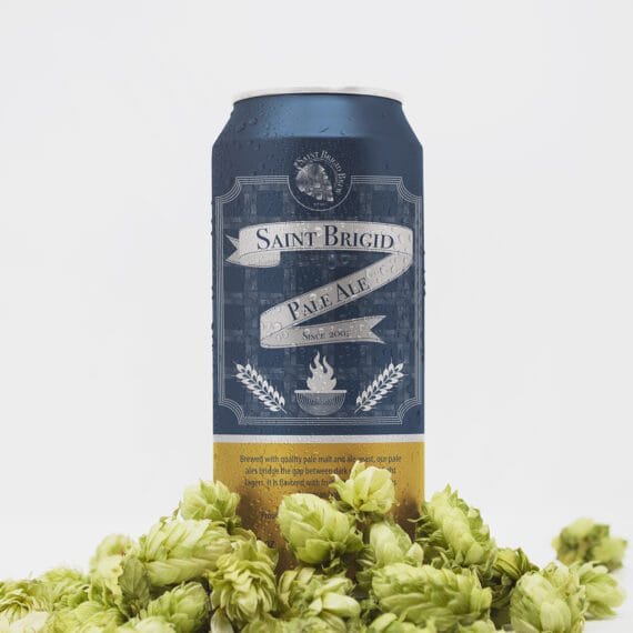 Saint Brigid Pale Ale can with navy and gold label standing upright among fresh hops on a white background