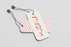 Two Husala hangtags with black cords: a pale vertical tag featuring red logotype overlaying a patterned pink tag