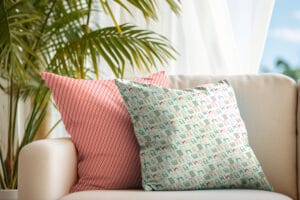 Decorative cushions with geometric red and pastel patterns on a beige sofa with a green plant in the background