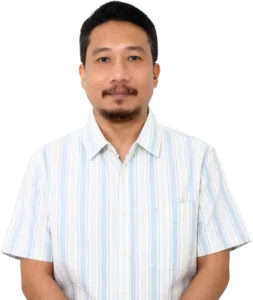 Chester Binalla with short dark hair wearing a light blue striped shirt standing against a transparent background