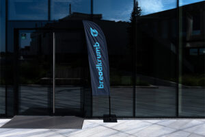 Glass office facade with a vertical blue flag displaying the Breadcrumb logo near the entrance.