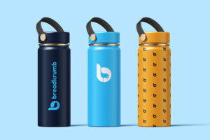 Three reusable water bottles in dark blue, light blue, and yellow featuring the Breadcrumb logo and patterned designs