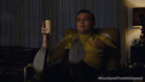 Leonardo Di Caprio pointing at the TV screen while sitting and drinking beer